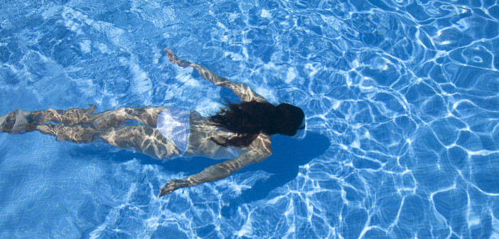 woman with white bikini diving at the bottom of a blue pool