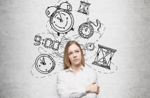 young pretty businesswoman thinking about time, in two minds, several models of clocks drawn behind. A concept of a value of time in business. Concrete wall at the background